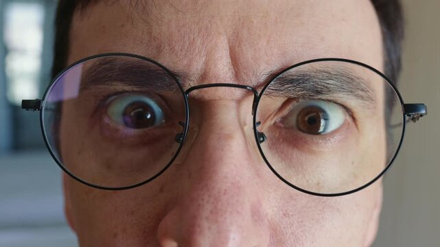 Man with round eyeglasses staring directly at the camera with a shocked and frightened expression. Extreme close up shot of his wide open eyes showing surprise, disbelief, and intense emotions