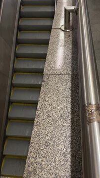Empty escalator steps topdown view of metal treads and speckled terrazzo ledge stainless handrail with tape mark, yellow safety edges and muted