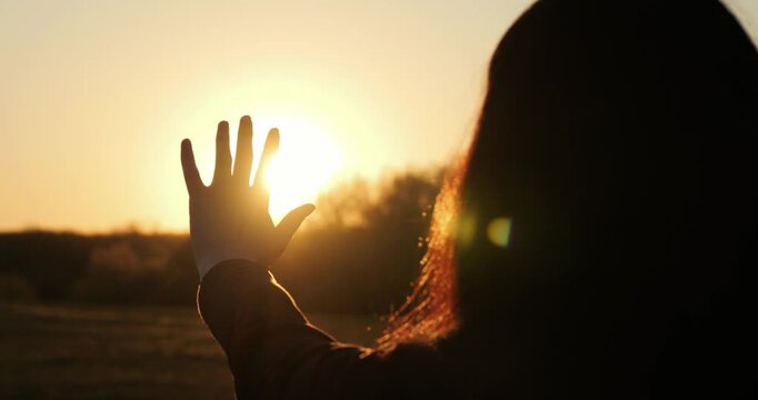 Silhouette of woman reaching hand toward sunset light. Concept of hope, inspiration and new beginning, emotional scene with warm sunlight and positive mood, horizontal video.