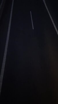 Empty highway lane lines at night, painted white markings on dark asphalt and occasional taillight flare from passing vehicle, cinematic solitude