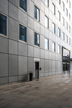Concrete facade and windows stretch along a quiet sidewalk, where urban architecture and building repetition create exterior daylight perspective