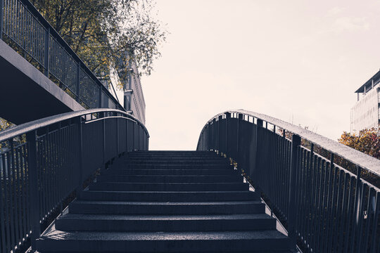 Concrete staircase and railing lead through a raised walkway, where urban architecture and building edges shape exterior daylight perspective