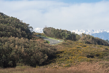 Fototapeta premium Winding Mountain Road Through Hills with Snowy Peaks