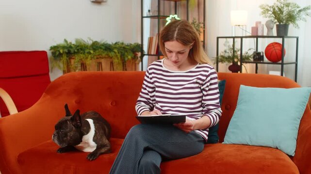 Middle-aged woman with French bulldog at home reviews dog sitter contract reads fine print confident. Girl with dog on sofa shows OK gesture agrees and signs paper form steady hand sure choice calm.