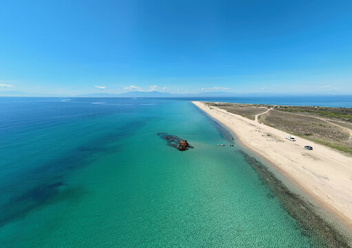 Aerial view of the Shipwreck Epanomi with its rusted hull resting in turquoise waters along a sandy beach under a clear blue sky in Epanomi, Greece.