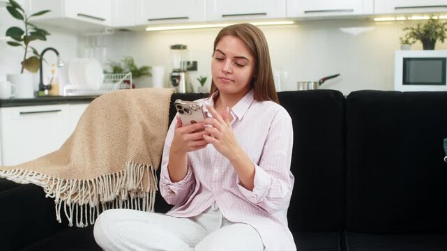 Young woman at home scrolls smartphone news feed feels fatigue sets phone down closes eyes breathes wants rest. Caucasian girl on sofa shows tired reaction mood detox break from screen for quiet time.