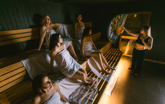 Female sauna master performing an aufguss ritual with a fan for a diverse group of women during a girls getaway