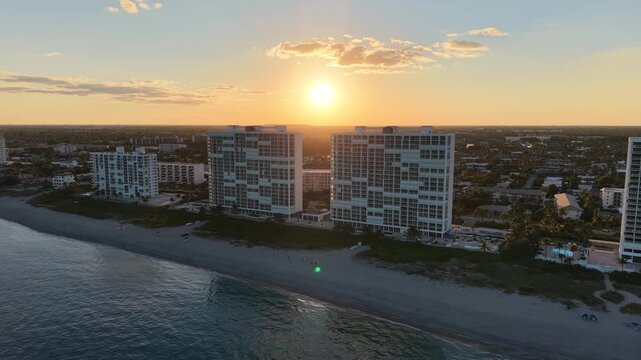 Drone pullback shot of Deerfield Beach Florida at sunset with the sun perfectly framed between two beachfront condo buildings golden sky and clear weather