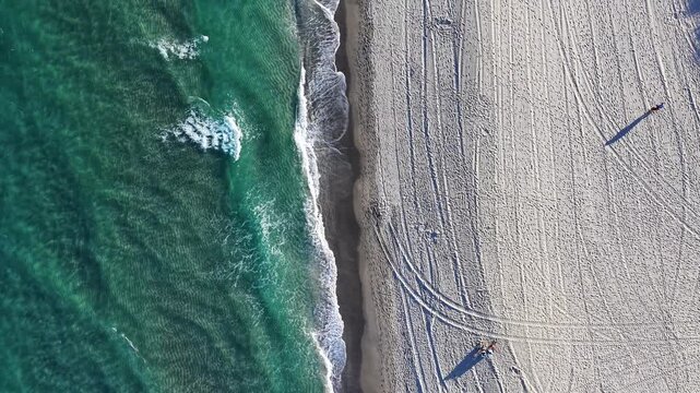 Straight down nadir drone perspective of ocean waves rolling in and breaking along the sandy shoreline at Deerfield Beach in Florida