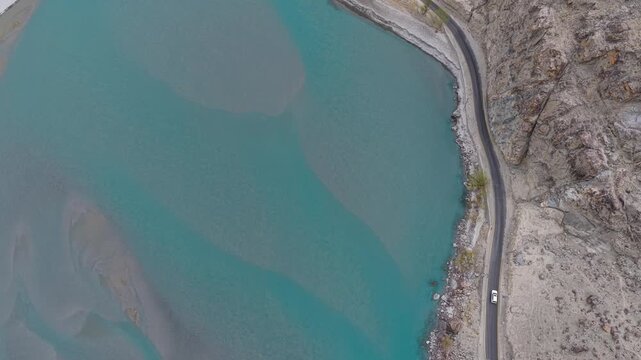 Cinematic nadir drone shot of a vehicle navigating the winding KKH in Northern Pakistan.