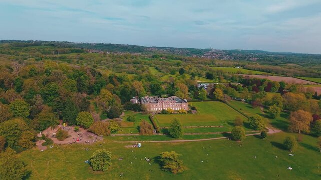 Cinematic aerial drone footage featuring a smooth rotating camera movement around a historic manor estate surrounded by trees, green parkland and countryside landscape. Scenic panoramic heritage archi