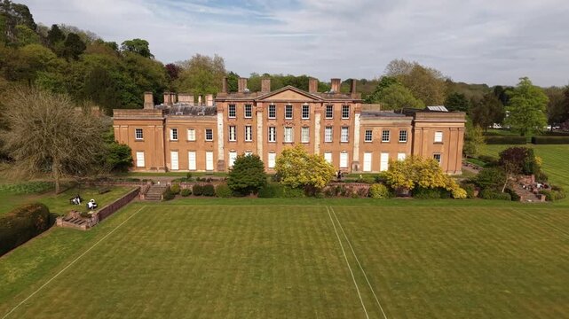 Smooth cinematic drone pullback from a historic manor house surrounded by landscaped gardens and countryside greenery. Elegant aerial footage revealing the estate and natural surroundings.