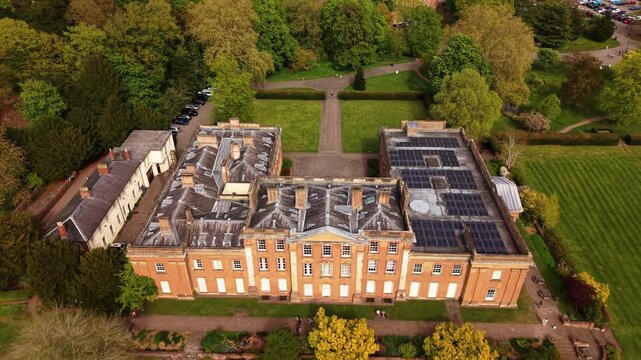Cinematic aerial drone footage pulling back from a historic manor house surrounded by landscaped gardens, trees and green parkland. Elegant countryside estate and luxury historic architecture viewed f