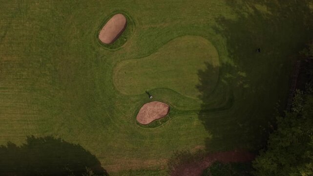 Top down aerial drone footage of golf course green with sand bunkers and fairway patterns. Cinematic overhead sports and leisure landscape with shadows and textured grass.