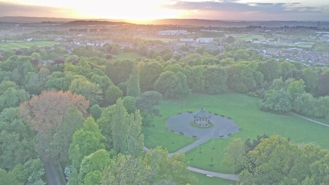 Historic bandstand sits within Locke Park in Barnsley, South Yorkshire, Yorkshire and the Humber, England, aerial drone shot above Victorian parkland, mature trees, and curving pedestrian paths during