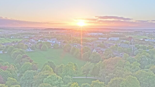 Locke Park and Barnsley stretch across South Yorkshire, Yorkshire and the Humber, England, drone forward flyover above mature woodland, residential districts, and glowing sunset atmosphere golden hour
