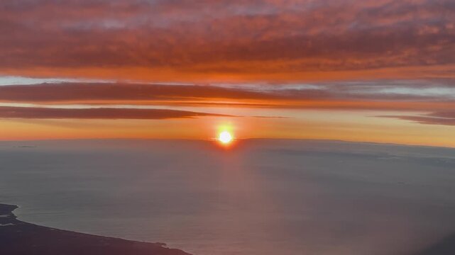 Aerial cockpit window view captured at sunrise from an airplane cockpit while flying on a coastal lanscape, with ethereal golden glouds.