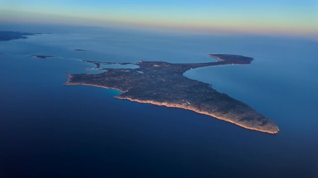 aerial spinning view taken from an airplane cockpit of Formentera island bathed by the warm sunset light, with a view of Ibiza island at the background.