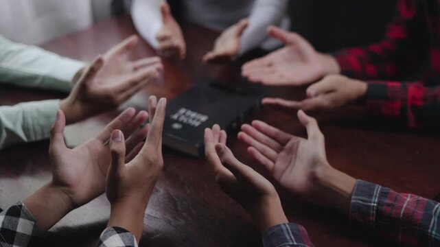 Group of Christian  holding hands praying worship together to believe and Bible on a wooden table for devotional for prayer meeting concept, teamwork.