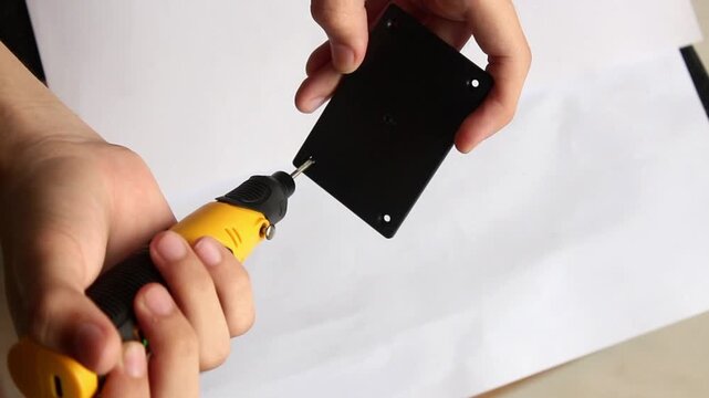 Close Up of Hand Using Portable Electric Drill to Make Screw Hole on Black Plastic Component