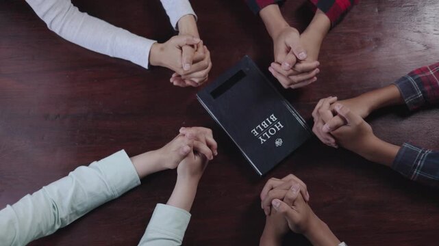 Group of Christian  holding hands praying worship together to believe and Bible on a wooden table for devotional for prayer meeting concept, teamwork.