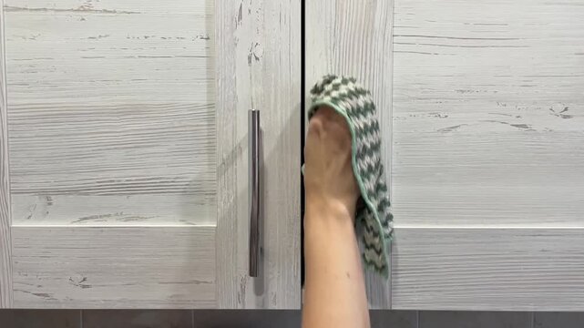 Hand wiping gray wood cabinet handles closeup, homeowner using patterned cloth to clean textured panels and metal pulls, soft natural light, methodical motions conveying tidy satisfying domestic chore