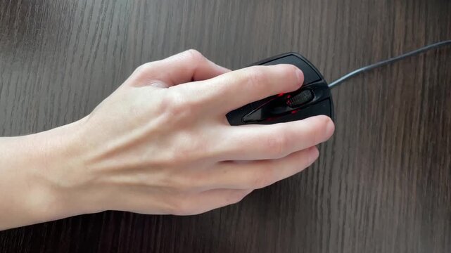 Closeup of hand manipulating mouse on desk. Precise hand grip on wired mouse during interface examination. Zoomedin view of hand expertly operating wired mouse on wooden office surface