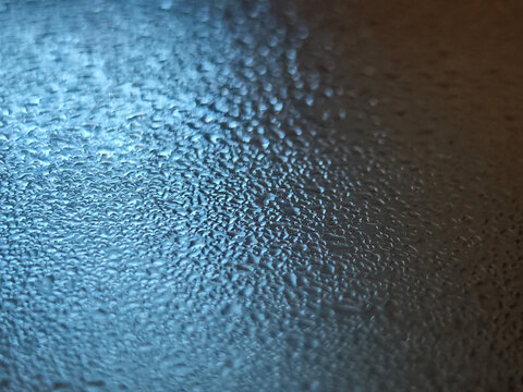 Macro shot of dense moisture condensation and tiny water droplets accumulated on a sleek surface with a dramatic metallic blue and dark copper color gradient