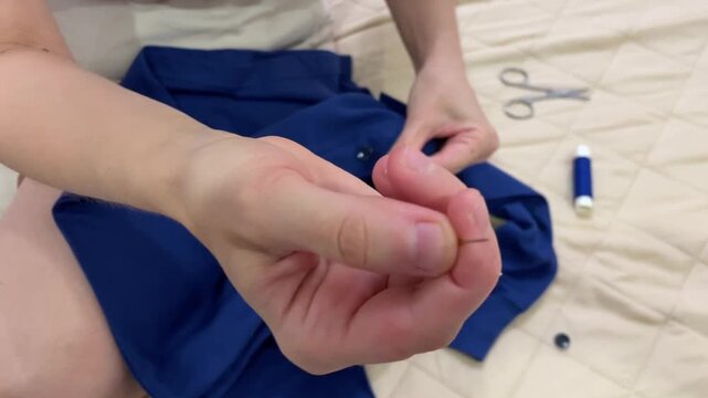 Woman repairs garment using needle and thread, Female artisan carefully stitching fabric with small scissors visible, Skilled woman focuses on mending blue piece with necessary sewing tools present