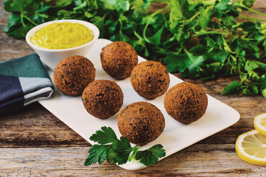 Falafel Plate with Dipping Sauce and Lemon Wedges on a Rustic Wooden Table