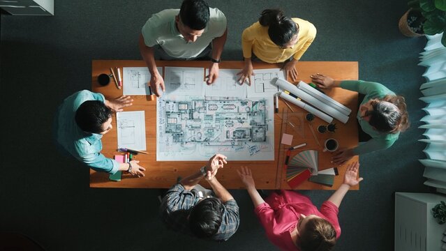 Top view of civil engineer team clapping hands while discussing idea at meeting table with color palettes and equipment. Top aerial view of diverse people applause to successful project. Symposium.