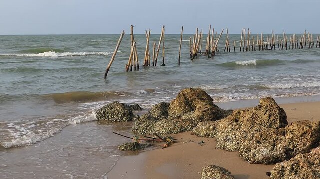 Mounds of rocks on the beach with a background of breakwaters made of bamboo hit by waves on the north coast of Tuban, East Java, Indonesia
