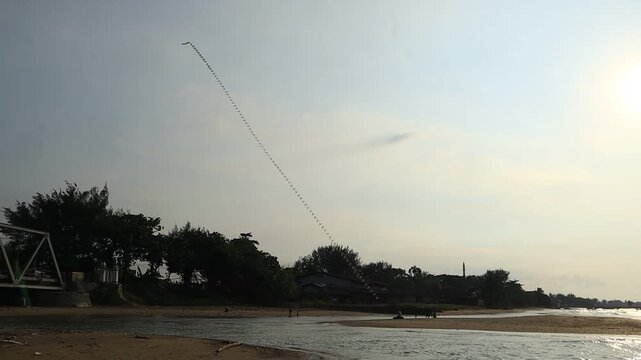 Long decorative kites snaking in the air, flown by a group of people on the north coast of Tuban, East Java, Indonesia