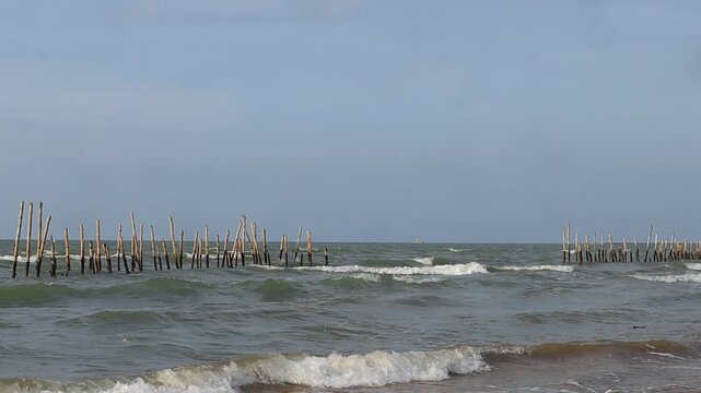 Waves break the beach past a breakwater made of wooden sticks on the north coast of Tuban, East Java, Indonesia