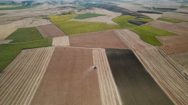 Aerial drone view of a tractor farming and plowing a patchwork of agricultural fields on a sunny day