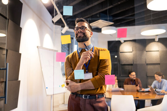 Creative manager brainstorming ideas using sticky notes on glass wall during office meeting