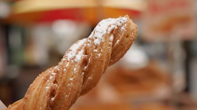 Close-up of a freshly fried, twisted spanish churro pastry dusted with powdered sugar, appetizing street food dessert