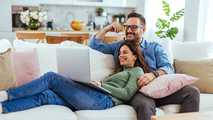 Obraz premium Happy Couple Relaxing on Couch With Laptop in Bright Modern Living Room at Home