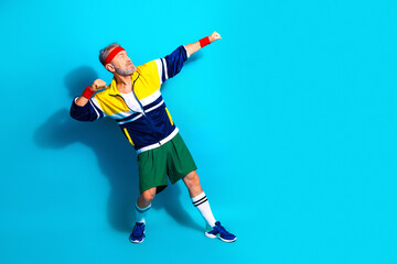 Obraz premium Energetic senior man in retro sportswear striking a victory pose against a bright blue background for fitness and active lifestyle