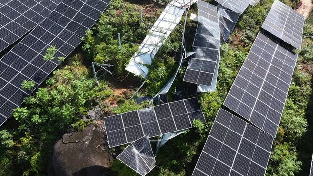 Aerial view of damaged solar panels installed on a rooftop with surrounding greenery