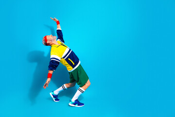 Obraz premium Active senior man stretching in retro sportswear on blue background — energetic fitness lifestyle and playful vintage workout pose