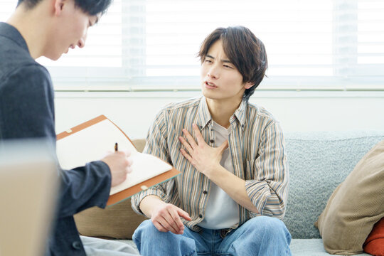 ソファに座ってカウンセリングを受ける若い日本人男性