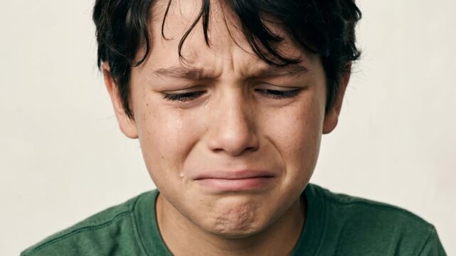 Close up of crying young boy with tears streaming down his cheek. Sad child expressing sorrow and pain