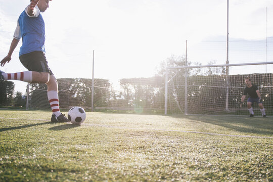 Football player kicking a ball in front of a goal with a goalkeeper