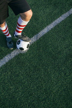 Legs of football player with ball on football ground