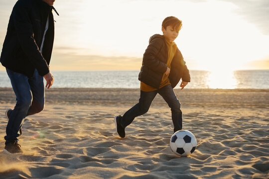 Father and son playing football on the beach at sunset