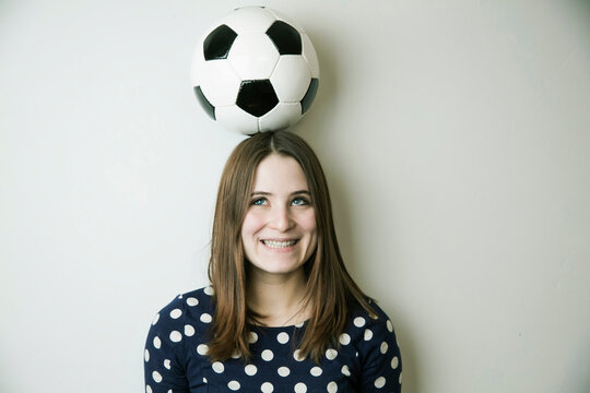 Portrait of smiling teenage girl with football on her head in front of white wall