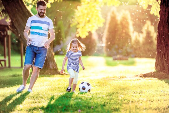 Happy little girl playing soccer with her father in a park