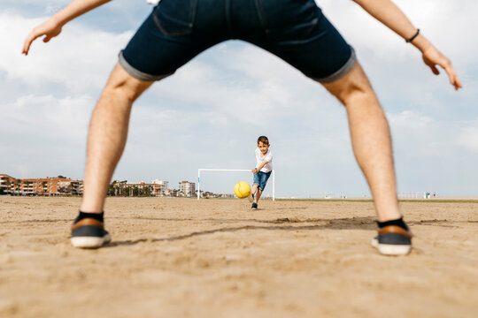 Man and boy playing soccer on the beach