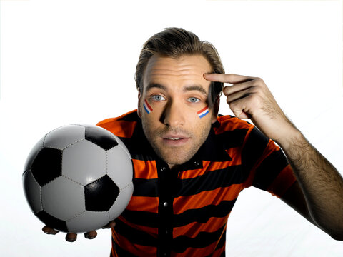 Man with Holland flag painted on face holding soccer ball, finger pointing on head